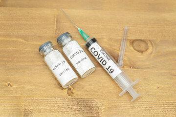 Two vials with coronavirus vaccine and disposable syringe on wooden background