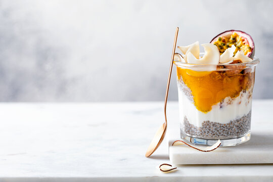 Healthy tropical fruit chia pudding with granola, mango, passion fruit and coconut chips in a glass jar. Vegan healthy breakfast, clean eating.