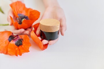 Natural organic cosmetics in glass bottle with red poppy flower in woman's hands