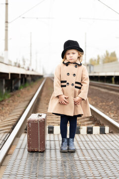 Girl in antique clothes with a suitcase on the railway tracks waiting for her train