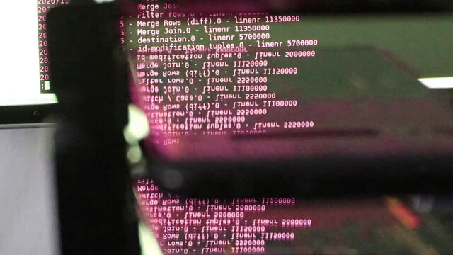 Red computer software code moving on a black monitor reflect on glass. Abstract computer hacking in process with rack server base, dynamic text running and flowing on pc screen