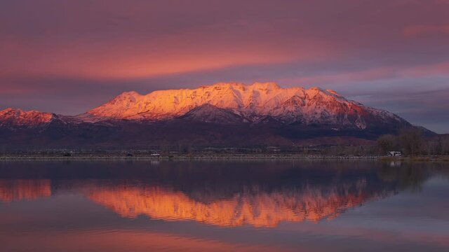 Snow capped Timpanogos Mountain glowing at sunset reflecting in Utah Lake as the water surface slowly ripples.