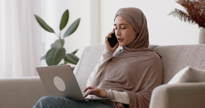 Remote work and freelance concept. Young muslim lady consulting client by phone, browsing on laptop