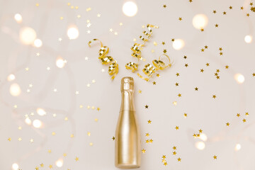 Creative Christmas and New Year composition with golden champagne bottle, confetti stars, party streamers and holiday decoration on beige and Set Sail Champagne background. Flat lay
