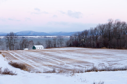 Dawn rural winter landscape with small sheds in field on St. Lawrence River coastline and the Laurentian mountains in the background, Saint-Vallier, Quebec, Canada, Quebec, Canada