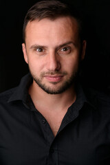 Studio portrait of a young caucasian man in a black blazer, looking at the camera, standing against plain studio background