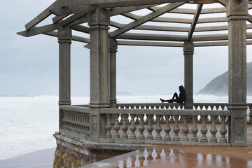 Woman sitting on a porch looking to the waves in the sea on a rainy day