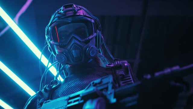 Female soldier of future in fiction helmet holding assault gun in her hands lit with blue neon street lights. Woman combat cyborg in futuristic protective costume. Cyberpunk warrior at night