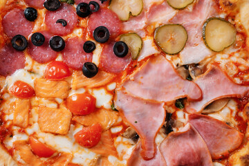 Italian pizza four seasons with ham, cucumber, olives and salmon close-up.  Italian fast food delivery.