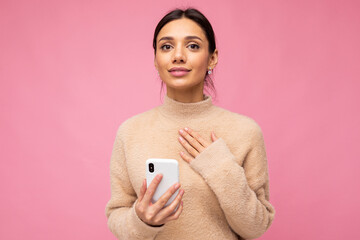 portrait of a gentle brunette on a pink background. holding a phone, looking at the camera