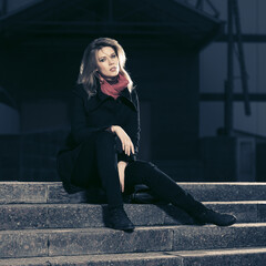Fashion blonde business woman in black coat sitting on steps