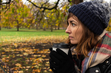 Fototapeta na wymiar Attractive young female drinking a coffee during a cold autumn morning in a park in central London, United Kingdom