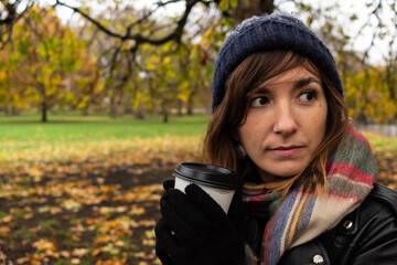 Attractive young female drinking a coffee during a cold autumn morning in a park in central London, United Kingdom