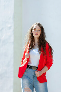 Glamorous Young Woman In Red Blazer In Jeans Posing Near White Wall