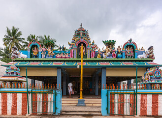 Kadirampura, Karnataka, India - November 4, 2013: Sri Murugan Temple. Yellow flag post in front of Mandapam with colorful statues on roof under gray cloudscape. 