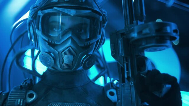 Portrait soldier of future in fiction helmet holding assault gun in her hand backlit with blue neon street lights. Female combat cyborg in futuristic protective costume. Cyberpunk warrior at night