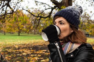 Attractive young female drinking a hot chocolate during a cold autumn morning in a park in central London, United Kingdom