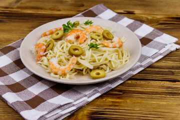Spaghetti pasta with prawns, green olives and parsley on wooden table
