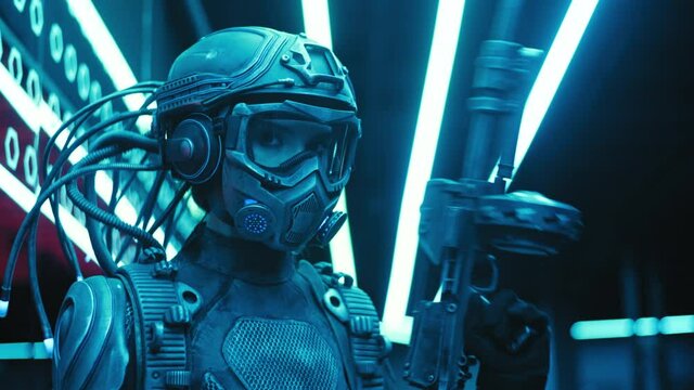 Portrait military soldier of future in fiction helmet holding assault gun in hand lit with blue neon street lights. Female combat cyborg in futuristic protective costume. Cyberpunk warrior
