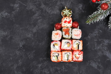 Herringbone made from fresh sushi rolls with sauce on dark, christmas new year food, traditional japanese cuisine, place for text, top view, banner for shop advertisement or invitation,