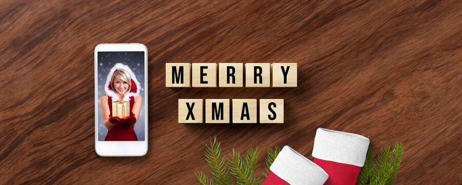 cubes with message MERRY XMAS and smartphone showing a Miss Santa on wooden background