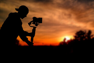 Silhouette of videographer is filming with cinema gimbal video dslr at sunset , professional video,...
