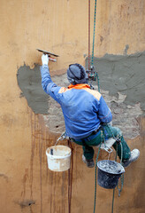 Plasterer on the wall of the house works with climbing equipment.