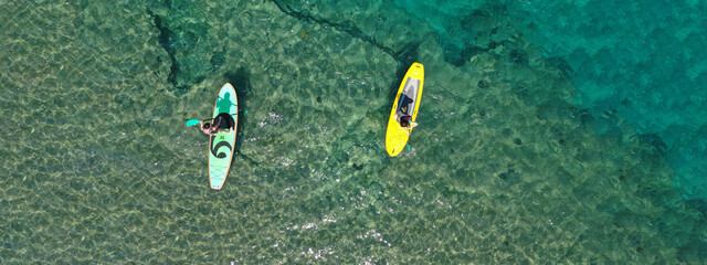 Aerial drone top view panoramic ultra wide photo of unidentified couple on a SUP or Stand Up Paddle board in tropical exotic sandy bay with emerald sea