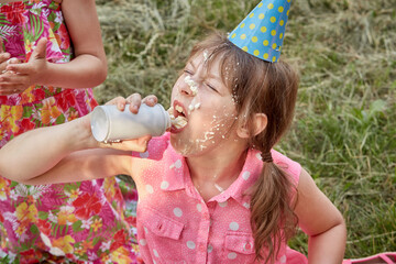 A girl with a dirty face in eating whipped cream. On the head of the party hat.
