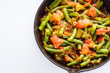 stewed green beans in a cast iron skillet on a white background