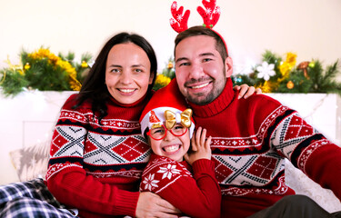 Happy family in christmas posing in red sweaters. Celebrating new year and christmas at home in 2021. Mom, dad and little daughter are having fun. High quality photo