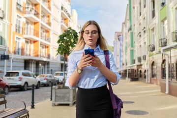 Young business woman with smartphone walking along city street
