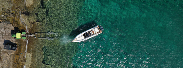 Aerial drone ultra wide top view photo of speed boat on trailer being towed by truck from emerald exotic sea to land