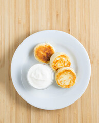 Cottage cheese pancakes with sour cream on the wooden background