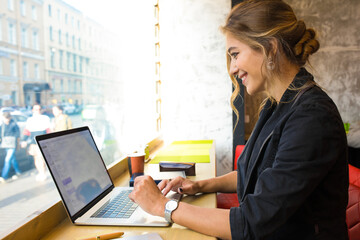 Happy smiling woman skilled blogger reading fashion article on website via laptop computer while sitting in coffee shop during recreation time