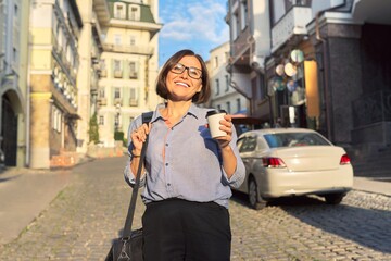 Fototapeta premium Mature business woman in glasses with office laptop bag walking along city street