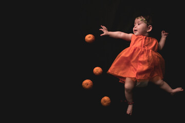 Niña pequeña en vestido anaranjado tratando de alcanzar una mandarina