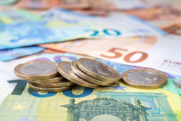 Fallen stack of coins on the euro banknotes background. Wealth, cash savings, accounting of income and expenses concepts. Shallow depth of field.