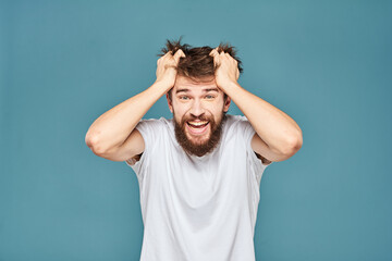 A bearded man in a white T-shirt gestures with his hands emotions blue background