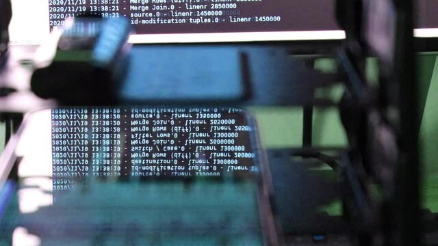 blue computer software code moving on a black monitor reflect on glass. Abstract computer hacking in process with rack server base, dynamic text running and flowing on pc screen