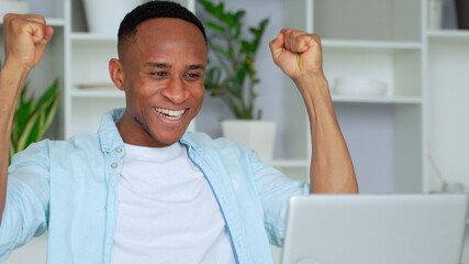 African-American feels happy received great news by internet looks at pc screen raised hands scream with joy celebrating on-line lottery win