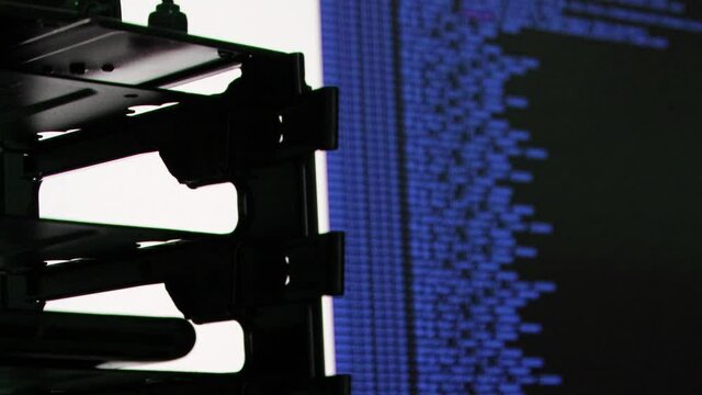 blue computer software code moving on a black monitor reflect on glass. Abstract computer hacking in process with rack server base, dynamic text running and flowing on pc screen