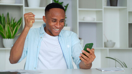 Young african american business man using phone and making winner gesture with fist in office