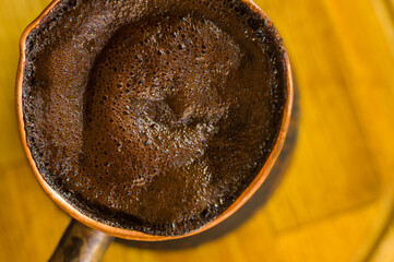 Natural coffee with thick foam, brewed in a copper cezve in the classical way, on a wooden background, macro photo.