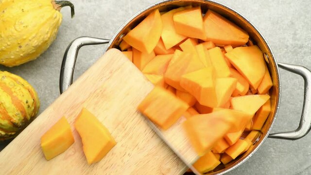 Woman adding chopped raw squash pumpkin to a pot, preparing pumpkin soup, top view