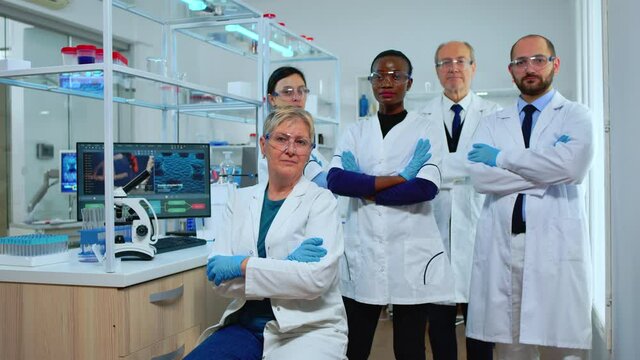Multiethnic team of experienced scientists looking at camera in modern equipped lab. Group of doctors examining virus evolution with high tech and chemistry tools for scientific research, vaccine
