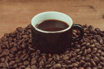 Vintage photograph of a cup of black espresso, accompanied by coffee beans on a wooden table