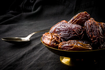 Big luxury dried date fruit in bowls on the dark surface, kurma ramadan kareem concept, close up.