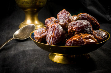 Big luxury dried date fruit in bowls on the dark surface, kurma ramadan kareem concept, close up.