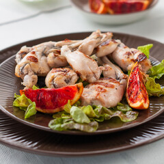 Grilled Frog Legs Garnished with Blood Orange Slices and Fresh Lettuce